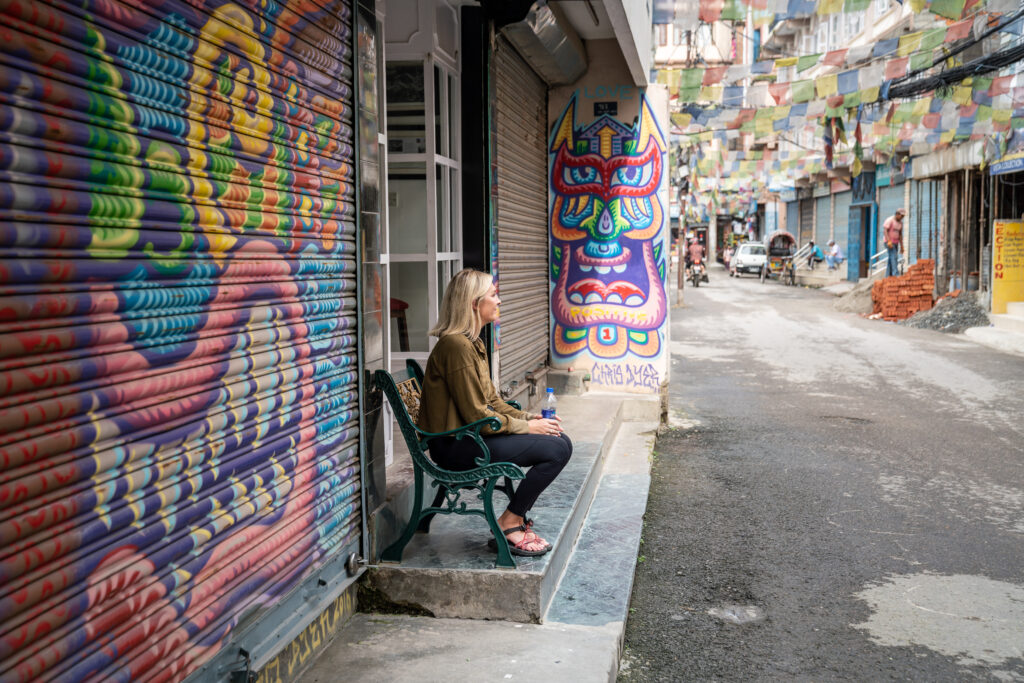 A tourist sits on a bench in the Thamel District of Kathmandu, Nepal surrounded by Chris Dyer graffiti art.