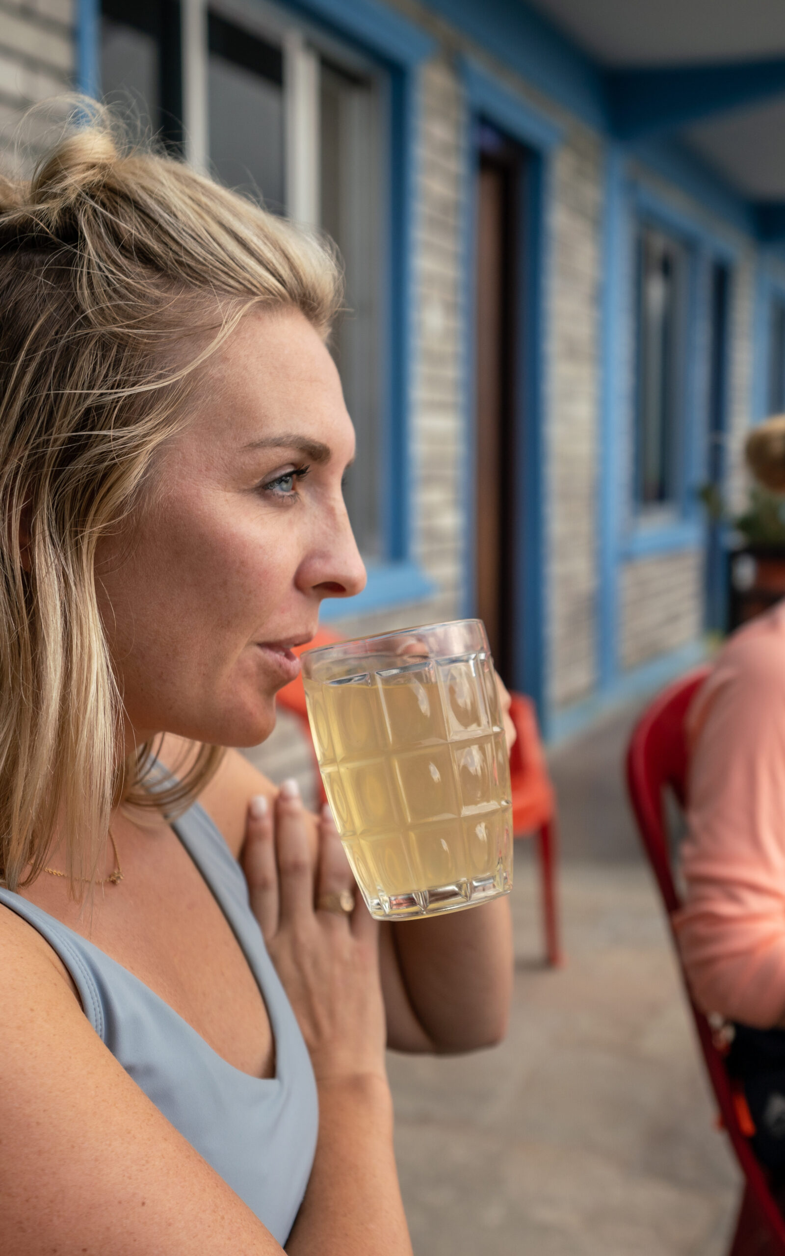A blonde woman drinks lemon honey ginger tea out of a glass mug.