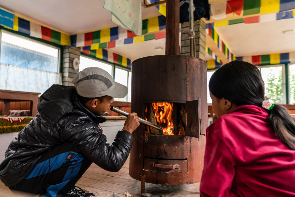 Two local Nepali youth lighting the wood stove inside the common room in a teahouse in the Himalayas.