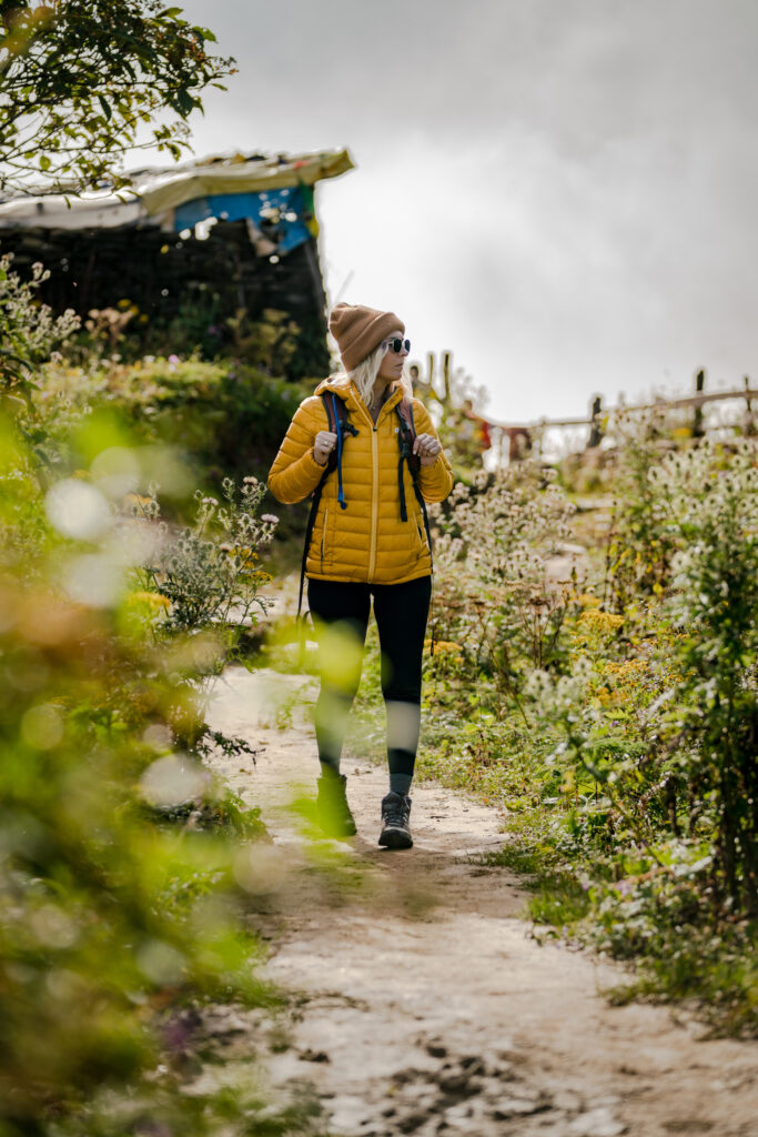 A blonde woman with sunglasses on and a yellow Sierra Designs down jacket walks do the trail.