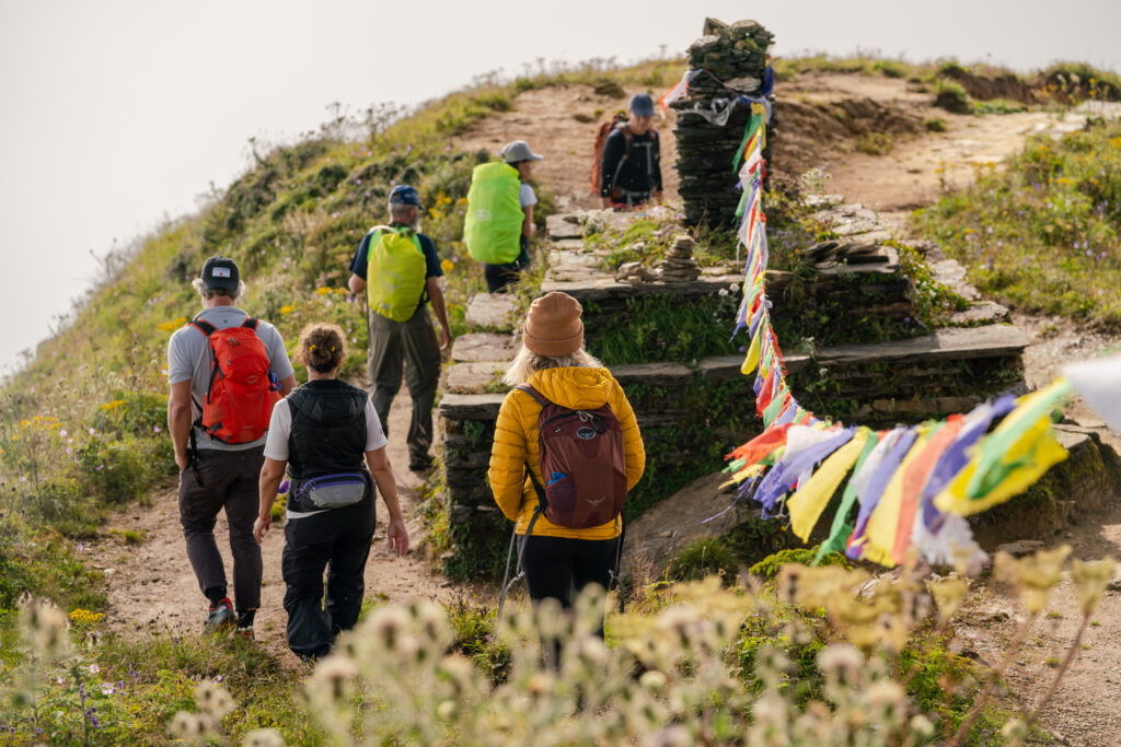 A group of hikers hike under prayer flags at the top of a pass in Nepal.