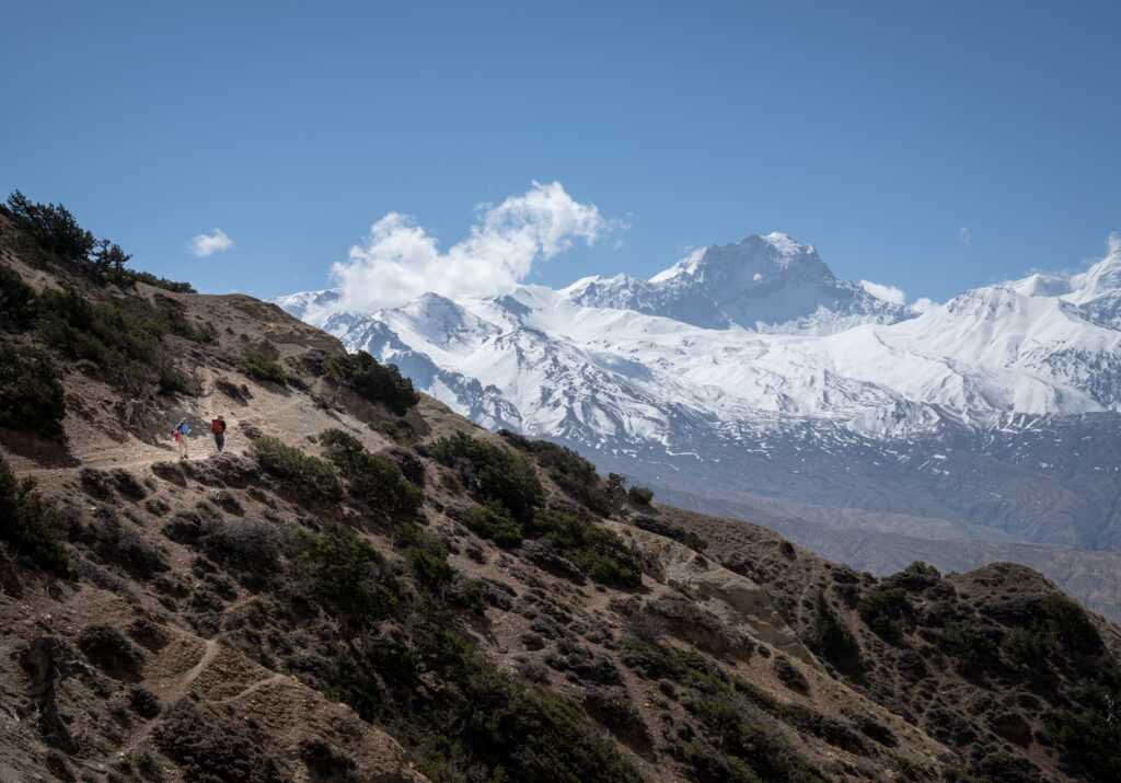 Two hikers on a high desert trail with sweeping and wide landscape views of the Himalayas in the background.
