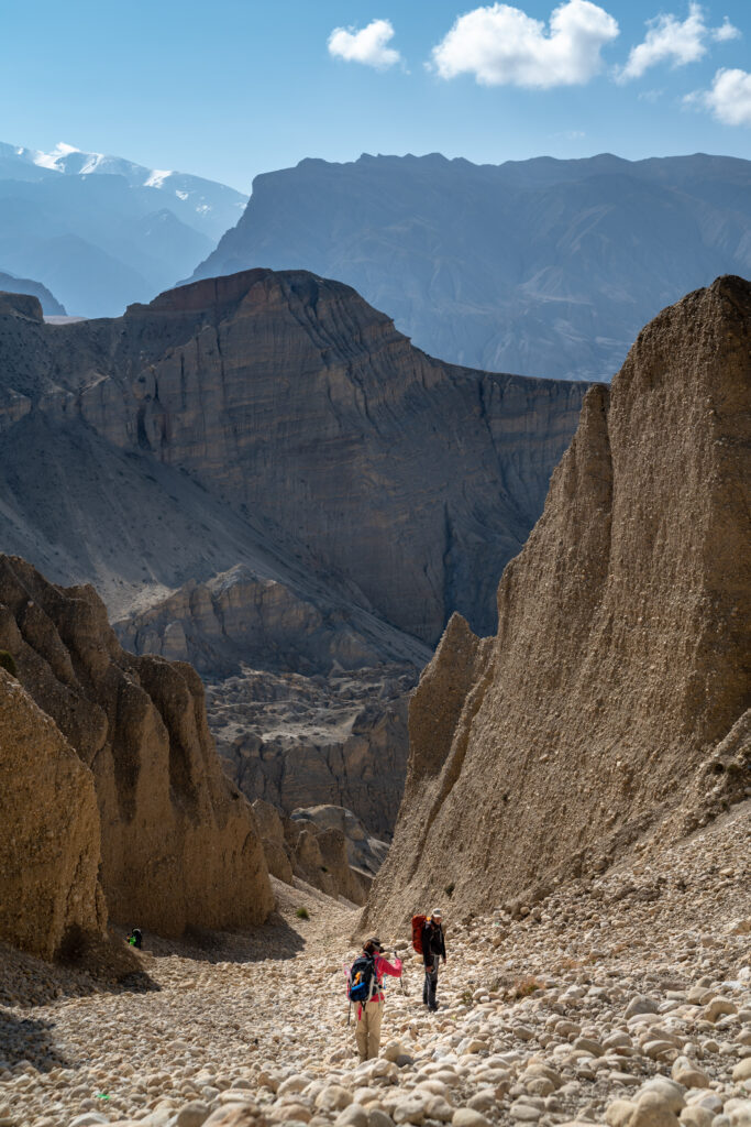 A woman and a man hike down a boulder filled canyon in Nepal.