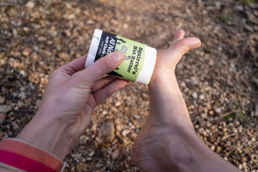 A hand applying anti-chafing salve onto the bottom of a foot in order to prevent blisters when hiking.
