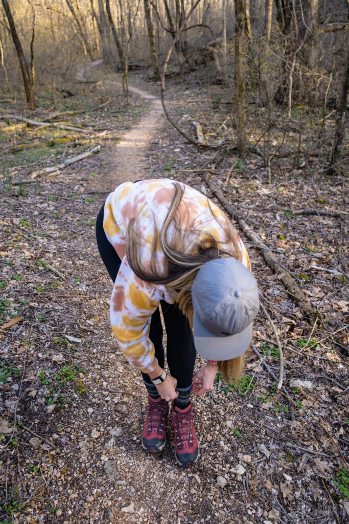 A woman bent down pulling up her socks while hiking.