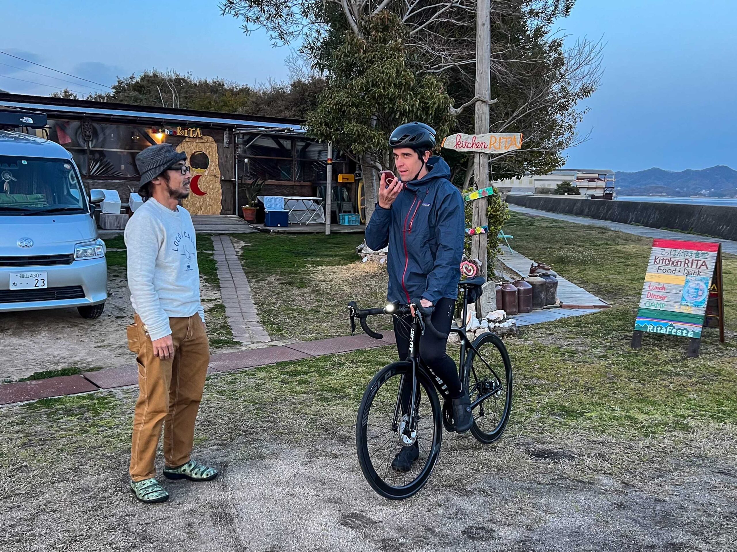 A male cyclist uses Google Translate on his iPhone to communicate with a local Japanese man on the Shimanami Kaido Cycling Route in the south of Japan.