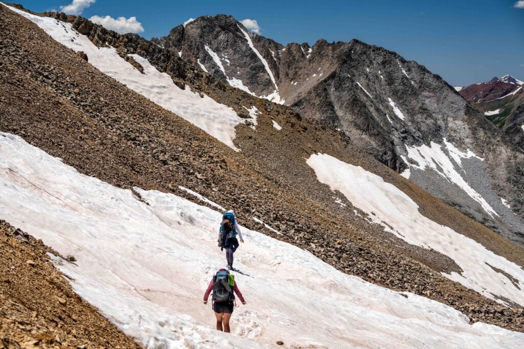 Two backpackers are traversing a small snowfield on the trail in Colorado.