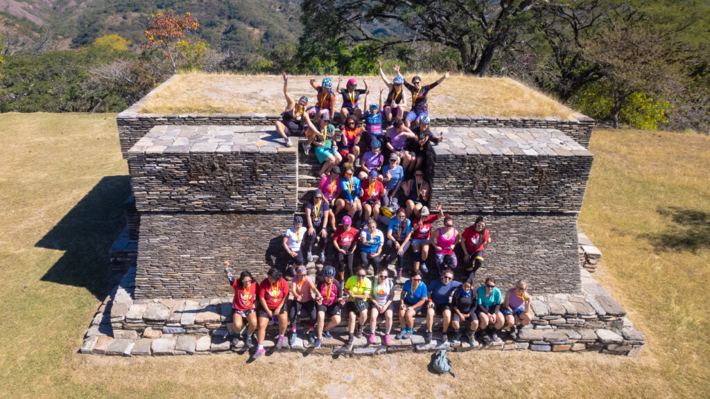 A large group of women mountain bikers small for a photo while sitting on ancient Mayan ruins in Guatemala.
