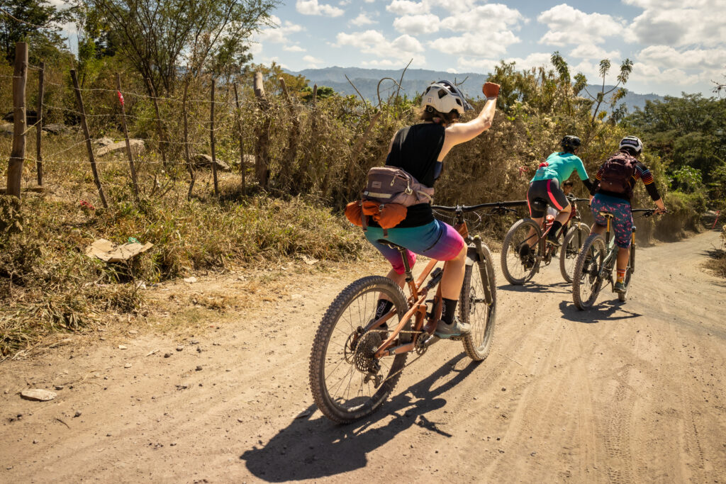 A woman cyclist lifts her fist in the air in celebration as she mountain bikes down a long gravel road.