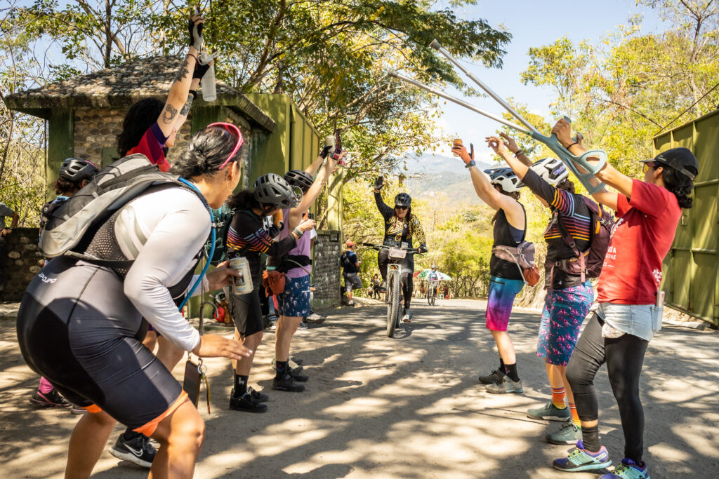 Women cheer and create a tunnel with their arms as a cyclist finishes a bike race.