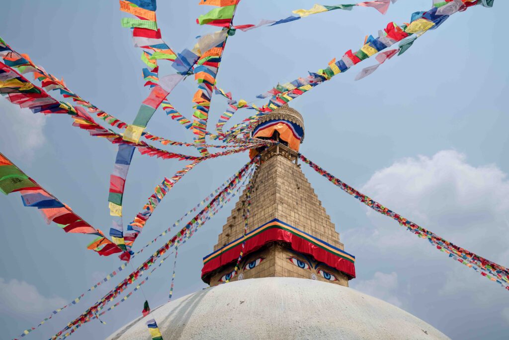 The top of the boudhanath stupa with prayer flags hanging and blowing in the wind from its top.