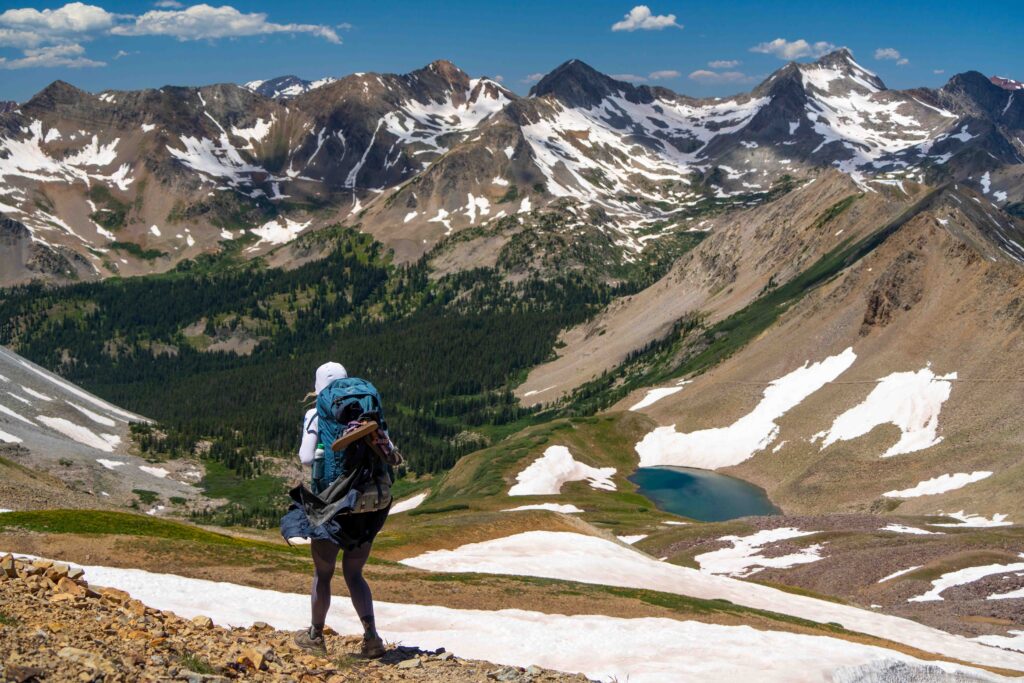 A backpacker hikes down the trail in Colorado with beautiful mountains in the background.